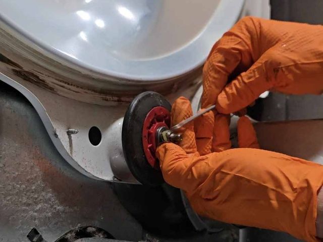 Gloved hands replacing a drum roller inside a dryer