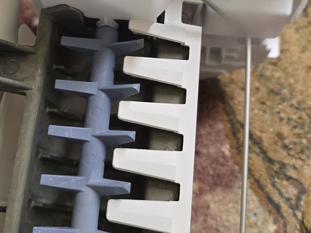Refrigerator ice maker assembly removed, showing the ejector arm and ice mold